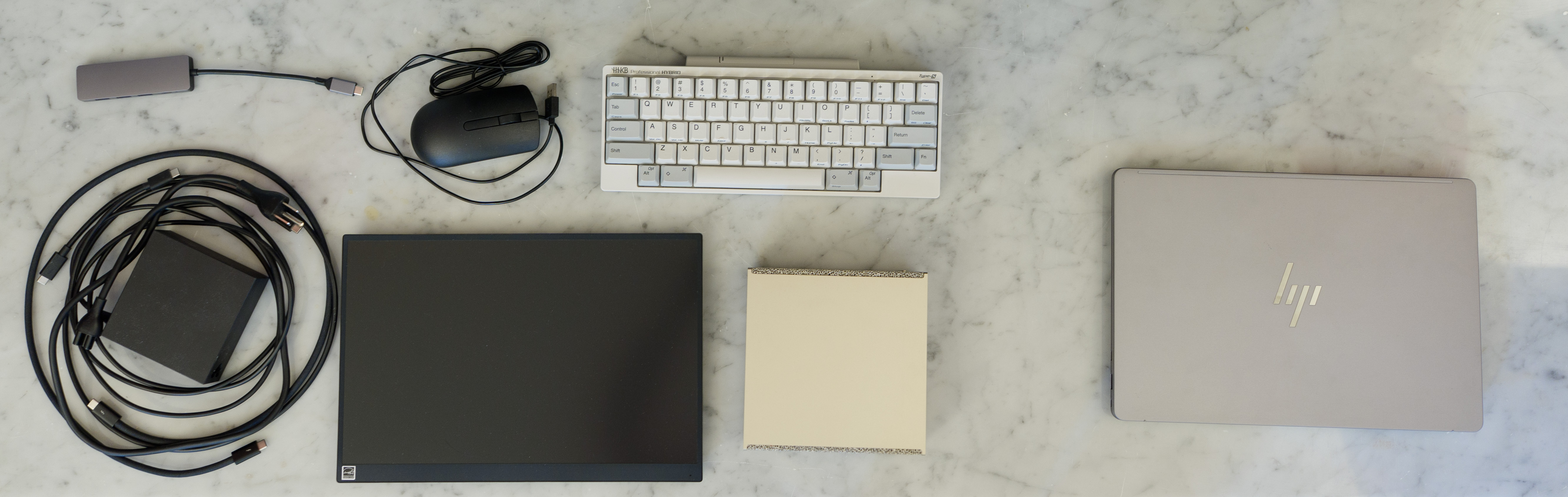 On the left, everything I needed to bring to demo with DGX Spark. A power brick, cables, VAIO portable monitor, wired mouse, USB-C hub, and HHKB keyboard alongside the gold DGX Spark.  On the right, the HP ZBook Ultra G1a -- 2 hours of battery life under load.